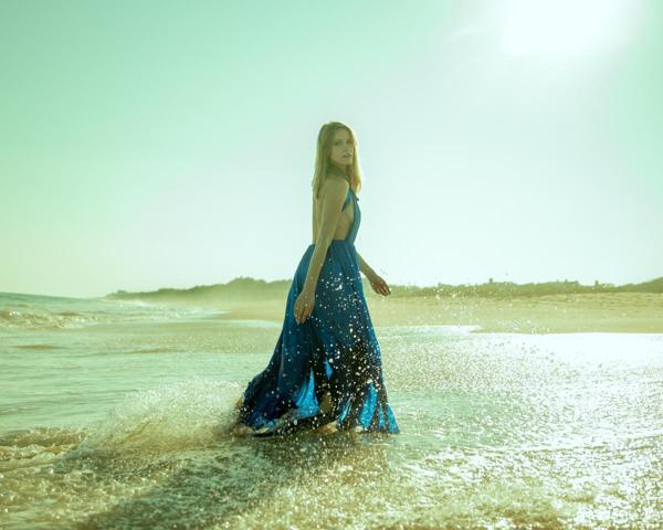 Caucasian female model in flowy blue gown walking through ocean wave photographed by Marty Gottlieb